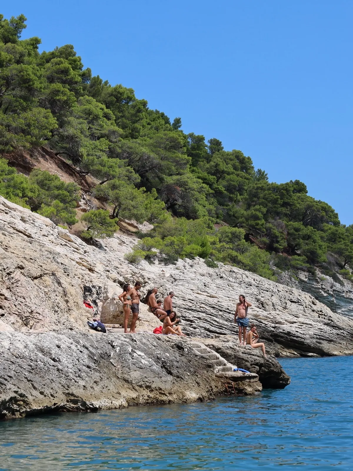 Costa adriatica — bagnanti lungo una costa rocciosa sotto il cielo estivo.