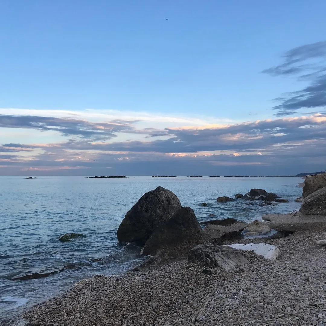 Spiaggia di ciottoli all'ora blu, con uno scoglio isolato sulla battigia.