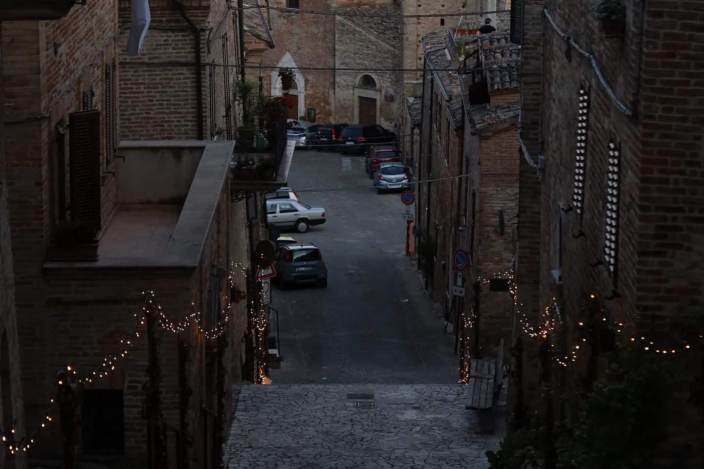 Vicoli in mattoni e luci serali in un borgo marchigiano.