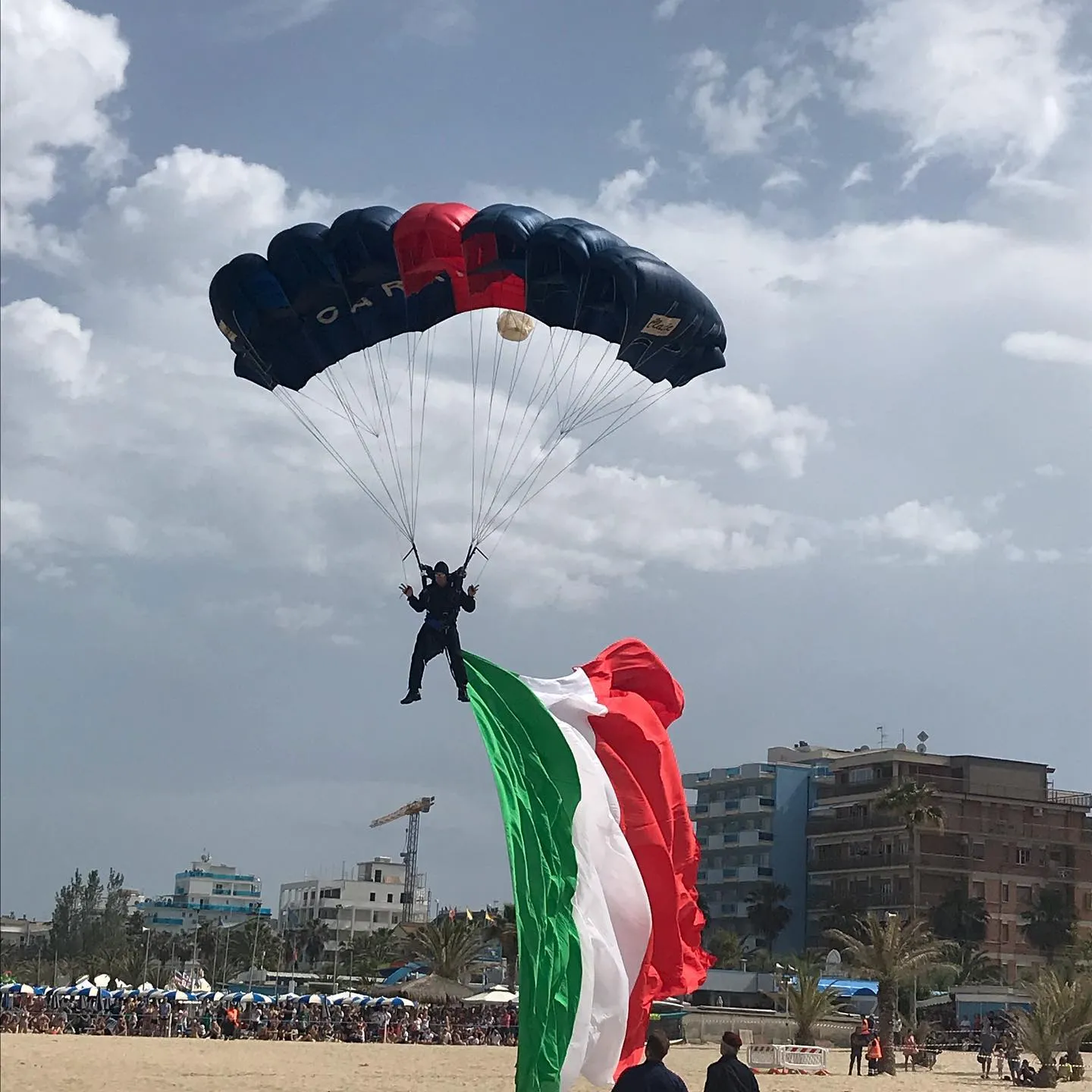 Paracadutista dei Carabinieri con il tricolore spiegato sopra il pubblico.