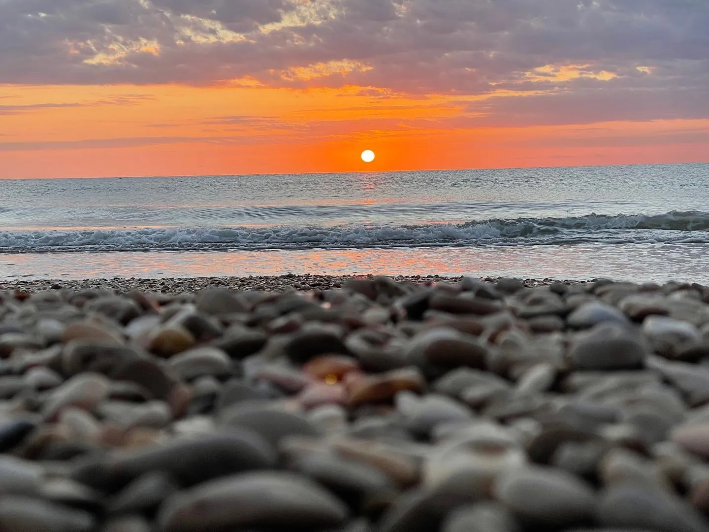 Tramonto sul mare visto dal livello della spiaggia, tra ciottoli e risacca.