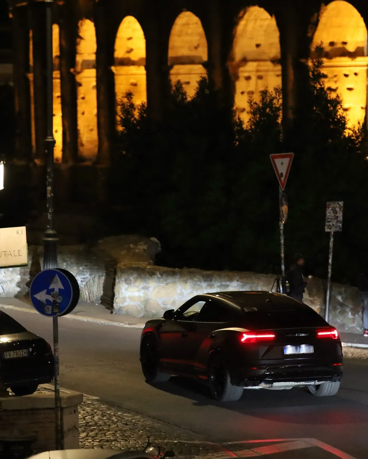 Roma — automobile sportiva in movimento con il Colosseo illuminato sullo sfondo.