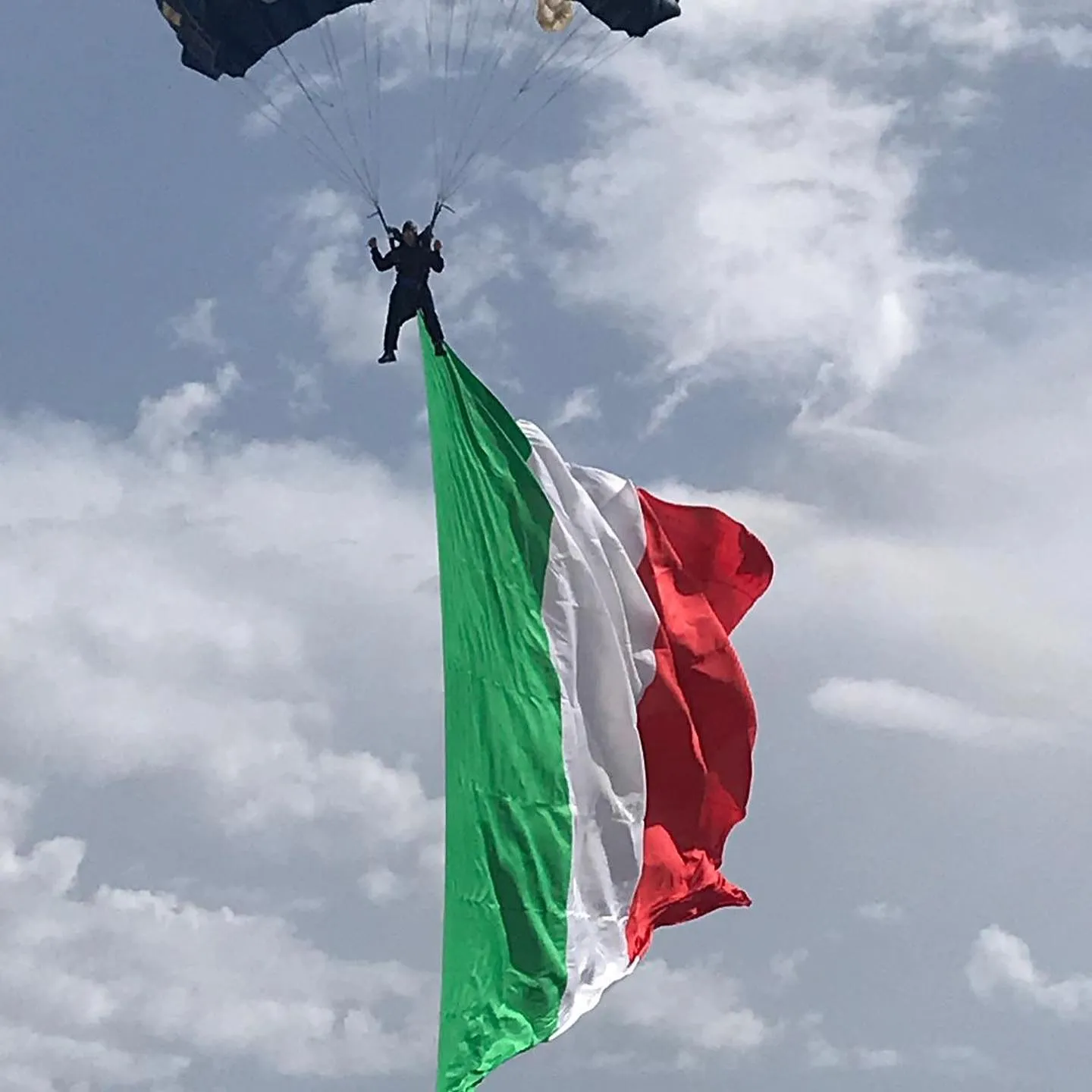 Paracadutista con grande bandiera italiana durante la discesa.