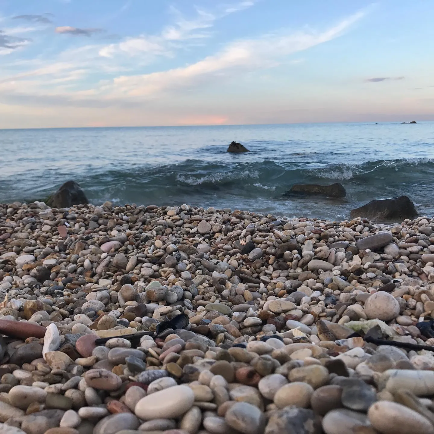 Riva adriatica — ciottoli in primo piano e mare in luce serale.