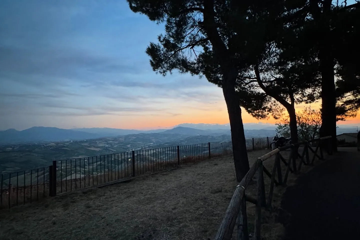 Panorama collinare al tramonto incorniciato dagli alberi.
