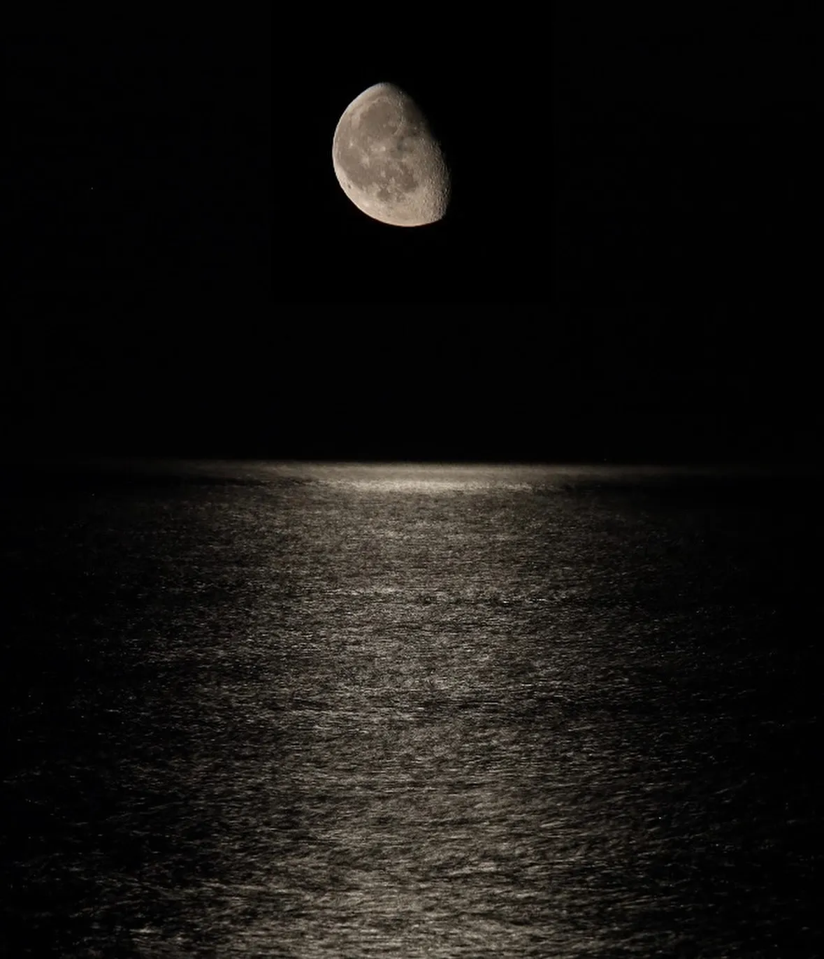 Luna sospesa sopra il mare, con il riflesso sulla superficie.