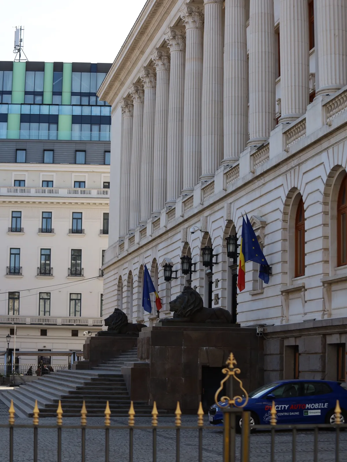 Bucarest — prospettiva urbana tra facciate istituzionali e bandiere.