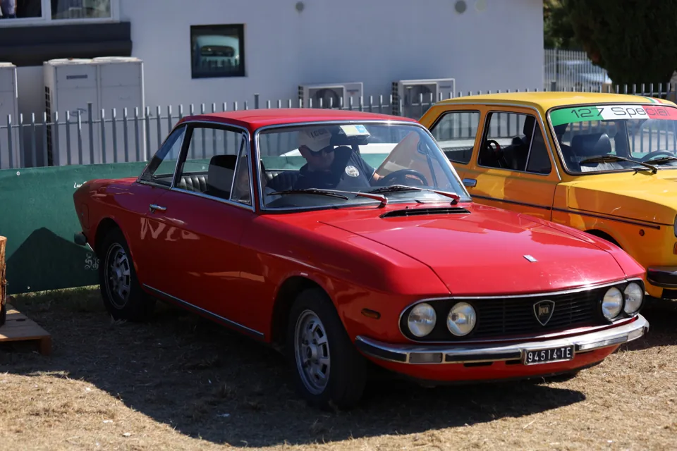 Una berlina rossa tra le auto esposte al raduno.